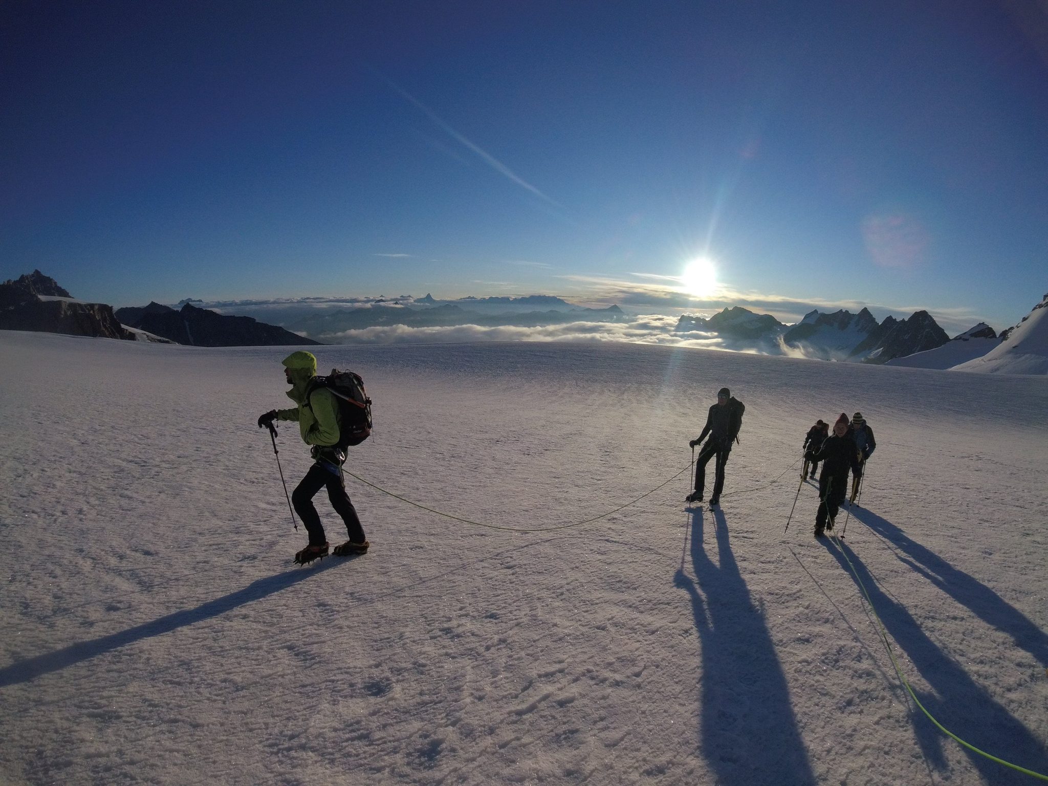 Alpinisti percorrono il ghiacciaio della Tribolazione legati assieme alla Guida Alpina. Sullo sfondo l'alba di una giornata magnifica