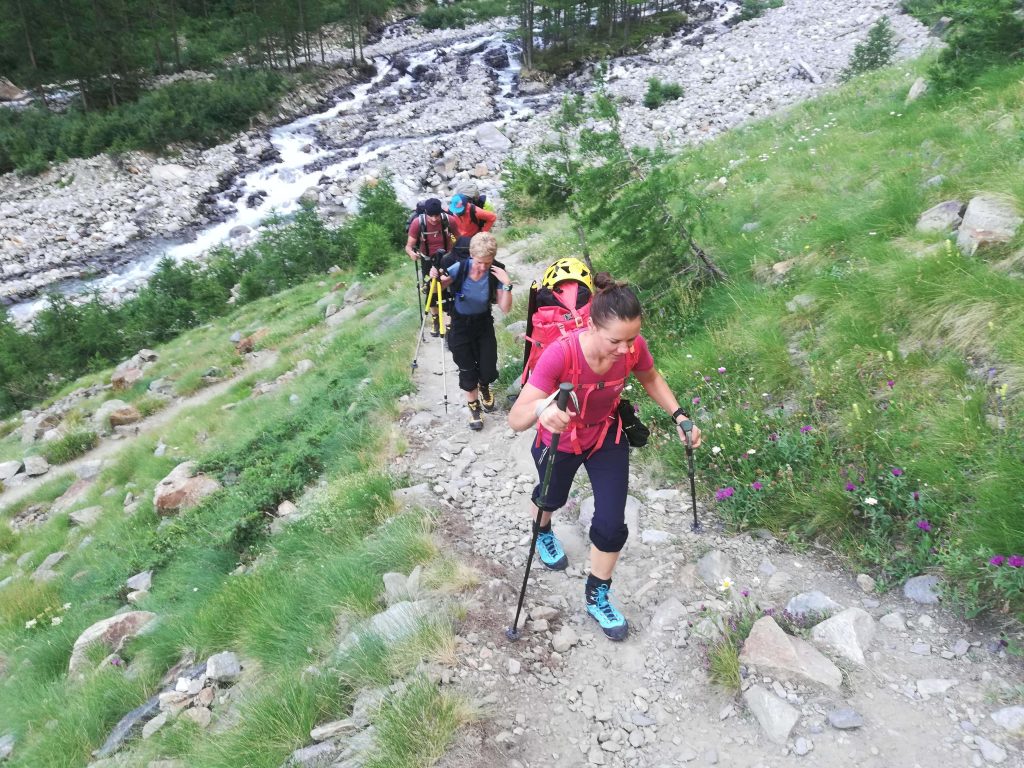 Alpinisti risalgono il sentiero verso il bivacco Grappein con la guida alpina. Sullo sfondo il torrente