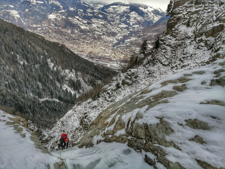 scalatore sale la cascata di ghiaccio del Mont Morion. Sullo sfondo la città di Aosta