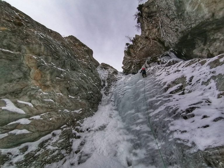 una guida alpina scala una cascata di ghiaccio incassata in una gola tra alte pareti di roccia