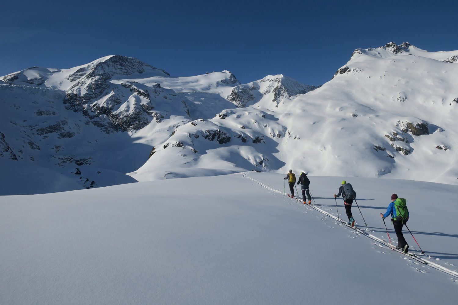 scialpinisti salgono un pendio con le pelli di foca. il paesaggio è imbiancato dalle forti nevicate e il cielo è blu.