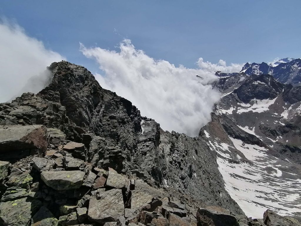 Cresta rocciosa. Sullo sfondo e sulla parte sinistra spesse nebbie si alzano. Ci sono ancora ampi nevai a base parete