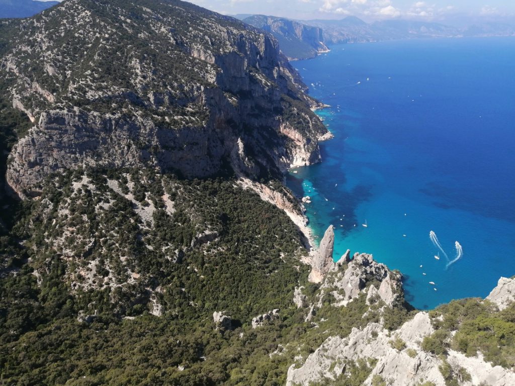 Dall'alto di una parete rocciosa si vede il mare blu con diverse barche