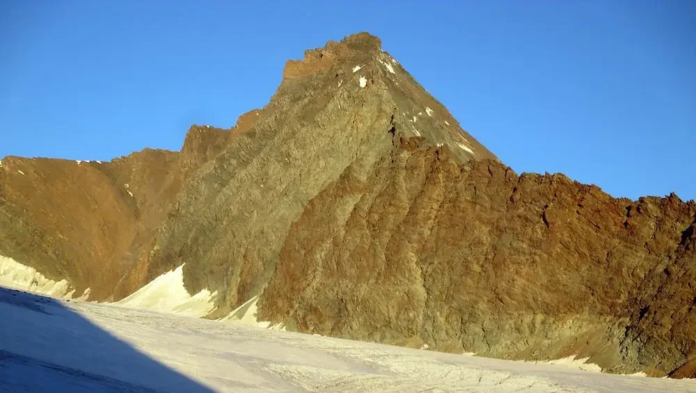 un vasto ghiacciao si estende alla base di una piramide rocciosa. Il cielo è azzurro senza nuvole