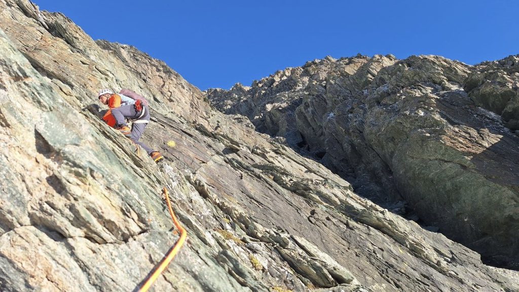 Parete rocciosa della Grivola su cui si vede un arrampicatore. Lo scalatore ha un casco bianco e una maglia blu e rossa, la corda a cui è legato è arancione. Sullo sfondo si vede un cielo terso, blu e senza nuvole.