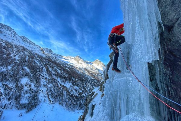 La Guida Alpina è intenta a scalare la cascata di ghiaccio Antares, in Valsavarenche. Sullo sfonfo un cielo azzurro e montagne innevate
