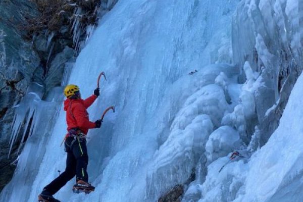 arrampicatore salte una cascata di ghiaccio utilizzando piccozze e ramponi